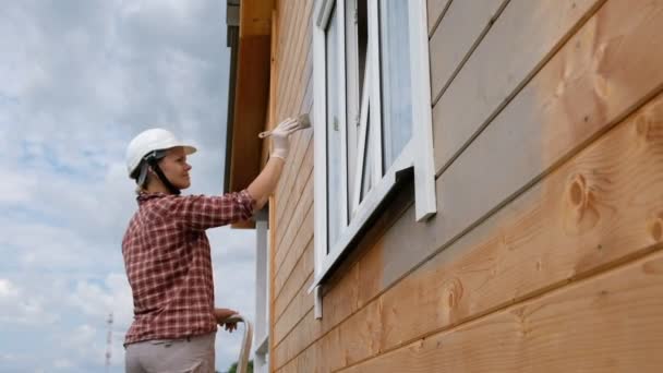 若い女性が新しい木造住宅の外壁を塗る カントリーハウスを塗装する過程 — ストック動画