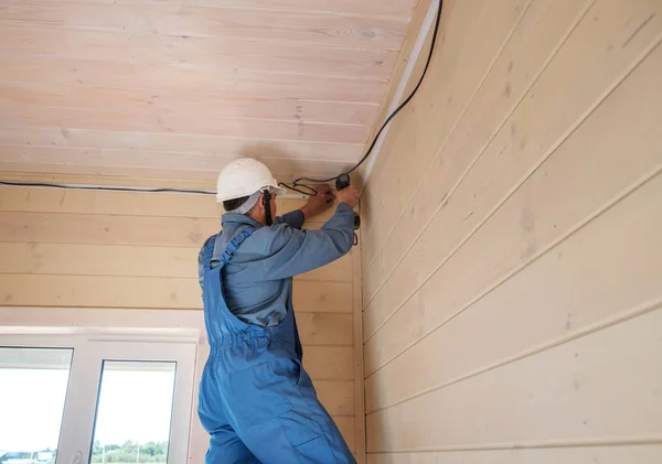 electrical engineer performs installation of electrical wiring in a new wooden country house