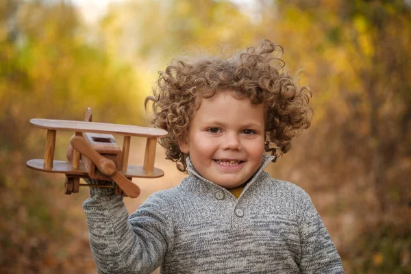 Милый Кудрявый Мальчик Играет Деревянным Самолетом Осеннем Парке — стоковое фото