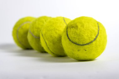 Close up image of bright yellow tennis balls arranged in a diagonal line on a clean white background