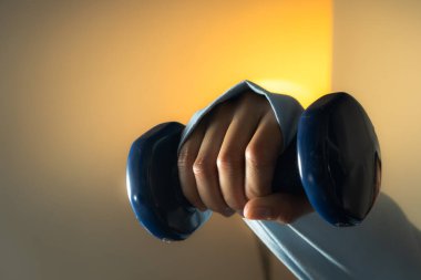 A person lifting a pair of dumbbells in a home at night setting, with soft indoor lighting