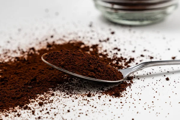 A spoon filled with soluble powdered coffee extract being scooped from a glass jar, isolated white background