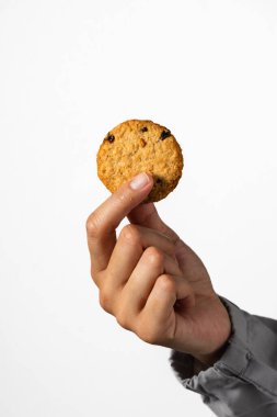 A close up of a hand holding a single golden cookie between two fingers against a plain background