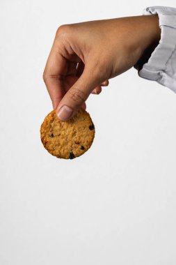 A close up of a hand holding a single golden cookie between two fingers against a plain background