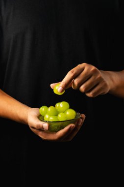 A close-up shot of a hand reaching out to pick green grapes from a bowl