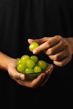 A close-up shot of a hand reaching out to pick green grapes from a bowl