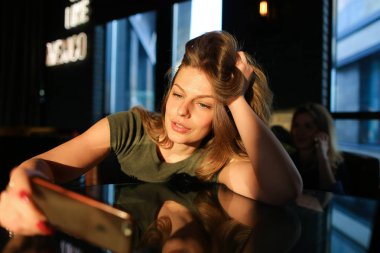 Smartphone kullanarak ve güneş ışınları kafede oturan güzel kadın.