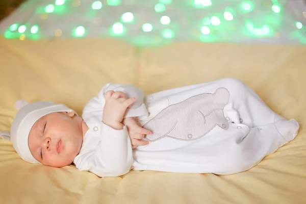 Little baby in white cap lying on blanket, green glares in background. — Stock Photo, Image
