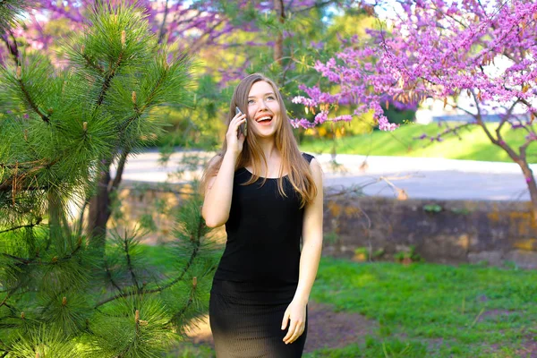 Hübsche Frau, die im Frühlingspark spazieren geht und per Smartphone spricht. — Stockfoto