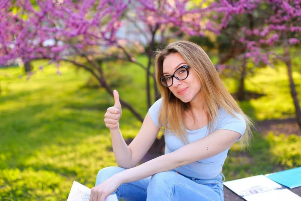 Studentka studovat v parku a ukazuje palec nahoru. — Stock fotografie