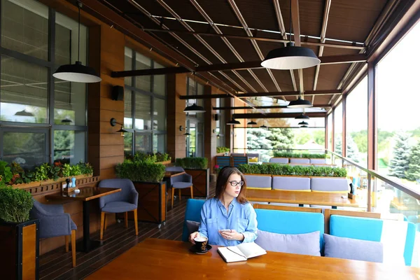 Estudiante en vasos bebiendo café en la cafetería y sentada con smartphone y portátil . — Foto de Stock