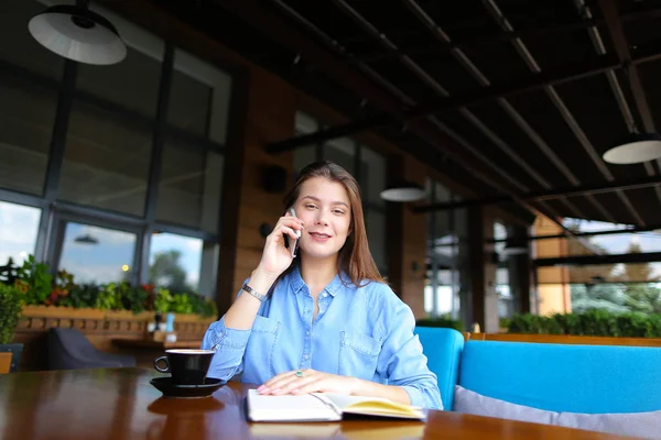 Mujer descansando en la cafetería con portátil y taza de café, hablando por teléfono inteligente . — Foto de Stock