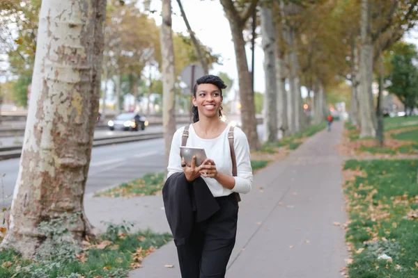 검은 색 여성 예쁜 학생을 사용 하 여 태블릿과 거리에서 산책 나무. — 스톡 사진