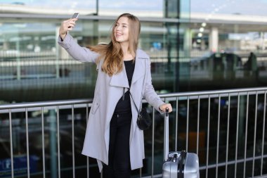 Genç kadın kişi smartphone valiz ve Havaalanı yakınında selfie yapma.