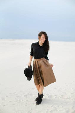 Kar üzerinde duran ve beyaz arka planda kahverengi etek, siyah bluz ve tutma şapka giyen büyüleyici kadın.