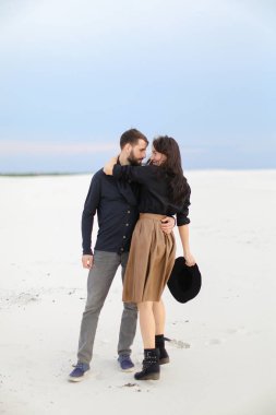 Hugginng kız etek giyen ve şapka, kış kar arka plan tutmak gülümseyen genç yakışıklı adam.