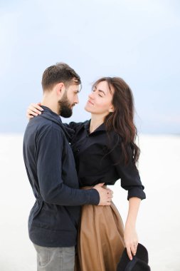 Genç çift sarılma ve beyaz kış arka planda etek giyen ve şapka tutmak bir kadın ayakta.