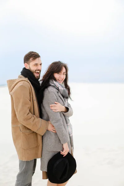 Glücklicher junger Mann umarmt weibliche Person mit grauem Mantel und Schal, weißem Winter-monophonen Hintergrund. — Stockfoto