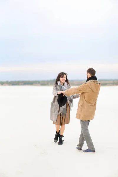 コートやマフラーを着た若い女性の男と雪の上を歩くと、手を握って. — ストック写真