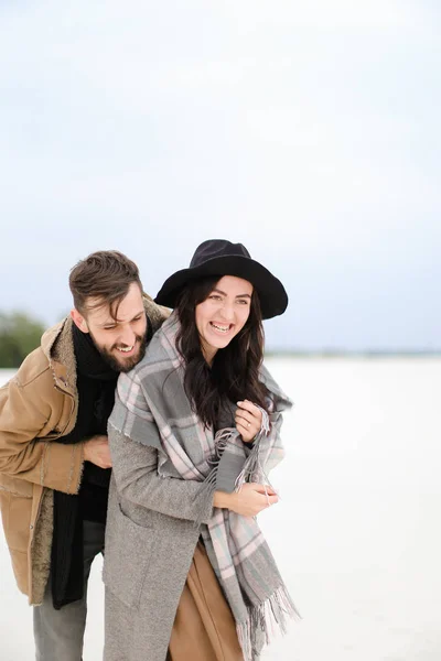 Leende kvinna och man med skägg bär kappor och scarfs stående i vinter snö bakgrunden. — Stockfoto