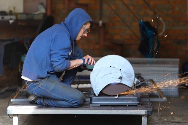 Mavi elbise giyiyor ve kıvılcım ile metal consturctions testere genç güçlü işçi.