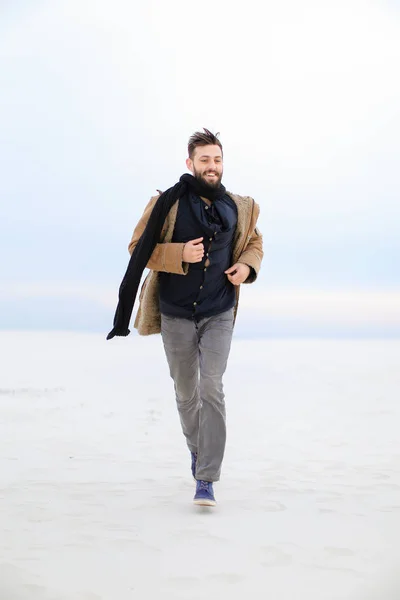 Caucásico elegante hombre feliz con abrigo marrón y bufanda corriendo en la nieve . — Foto de Stock