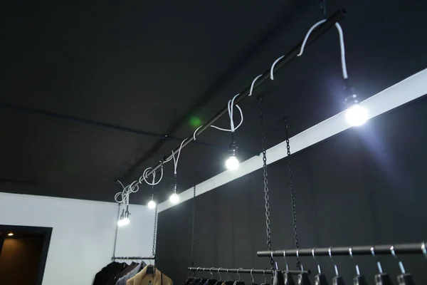 Hangers met kleding en lampen in de kast, zwarte plafond op achtergrond. — Stockfoto