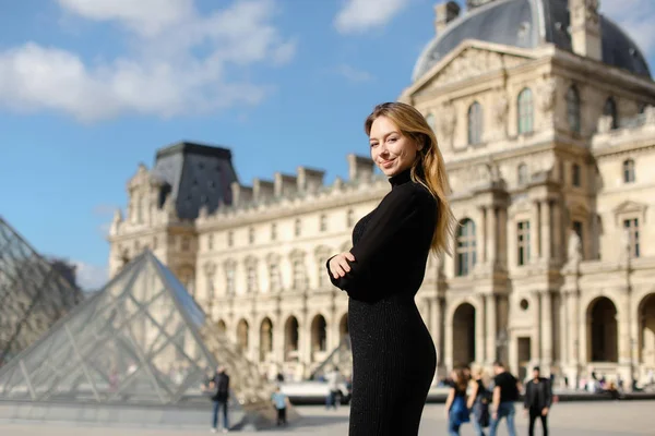 Hezká žena stojící poblíž Louvre a sklo pyramind v černých šatech v Paříži. — Stock fotografie