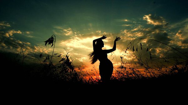 Female person dancing in steppe, silhouette in sunset background. Concept of dancing meditation and relaxing on nature.