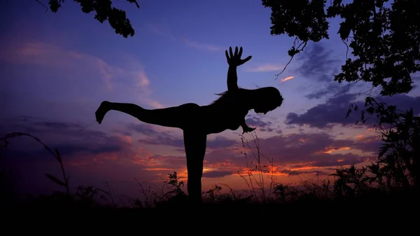 Silueta femenina negra haciendo yoga asana en fondo de cielo violeta . — Foto de Stock