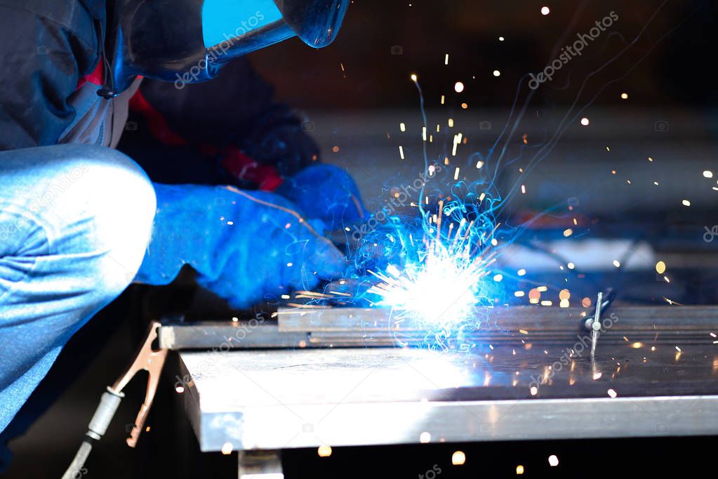 Male worker wearing construction gloves welding metall construction, blue welding arc.