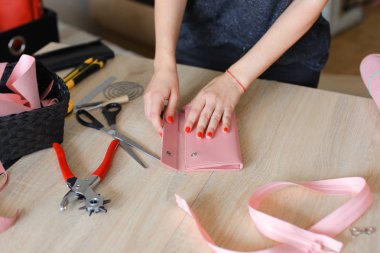 Female person making pink leather wallet with tools at atelier. clipart