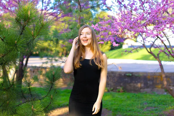 Beautiful female person walking in spring park and talking by smartphone. — Stock Photo, Image