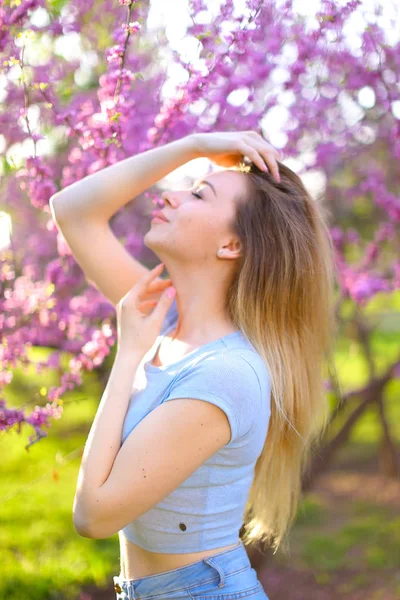 Junge blonde weibliche Fotomodell steht im Park mit Blütenhintergrund. — Stockfoto