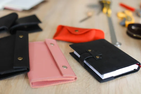 Stylish black and pink handmade leather wallets and notebook lying on table.