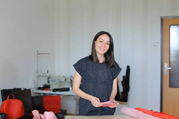 Mulher feliz fazendo carteira de couro rosa em casa atelier . — Fotografia de Stock