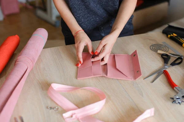 Creative female person making pink leather handmade wallet at home.