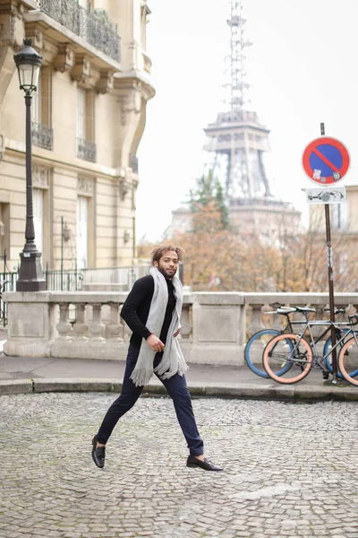 Afro Amerikaanse man in de buurt van verkeersbord en fiets met Eiffeltoren in achtergrond draait, het dragen van grijze sjaal en een zwarte trui. — Stockfoto