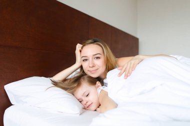 Küçük kızı ile sabah beyaz keten ile yatakta uyuyan genç kadın.