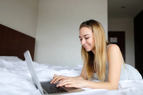 Chica joven usando el ordenador portátil y acostado en la cama por la mañana . — Foto de Stock