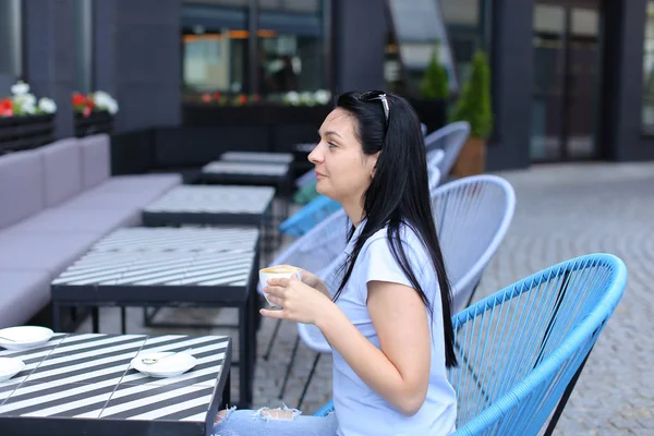 Schöne brünette Frau trinkt Kaffee im Café und sitzt im blauen Stuhl. — Stockfoto