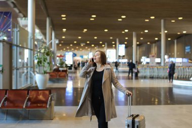 Kadın Avrupa kişi valiz ve smartphone ile konuşurken ile Havaalanı salonu gidiş.