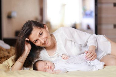 Yeni doğan bebek tutan ve beyaz elbise giyen altın bilezik ile genç beyaz anne.