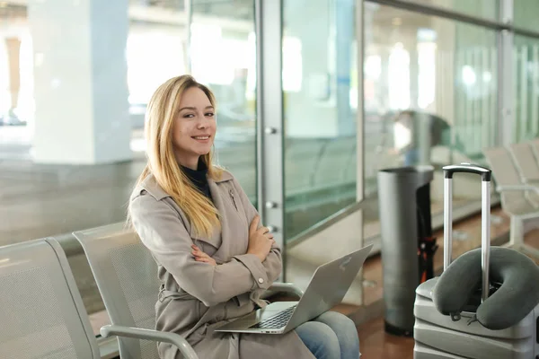 Kaukaski Ładna dziewczyna siedzi w poczekalni z laptopa w pobliżu walizka. — Zdjęcie stockowe