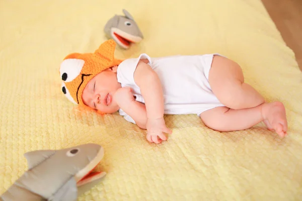 かわいい赤ちゃんおもちゃで黄色の背景の上に横たわると、オレンジ色のキャップを身に着けています。. — ストック写真