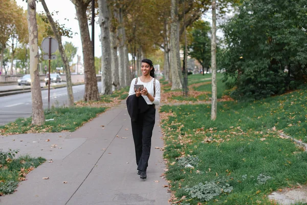 Afro americano bonita estudiante caminando con tableta en otoño parque, usando mochila . — Foto de Stock