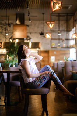Etnik kot giyen kafede ayakları ile sandalyenin arkasında oturan şık kadın.