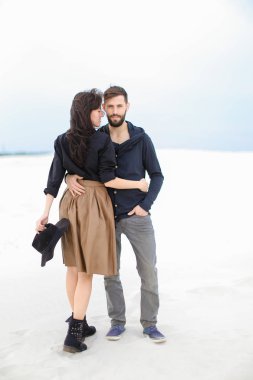 Genç çift birbirlerine sarılmak ve beyaz monofik kış arka planda moda giysiler giyiyor.