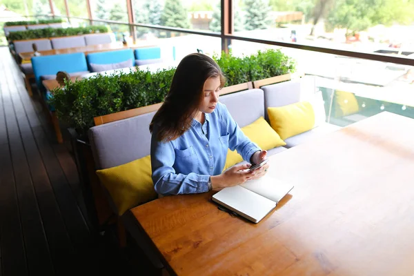 Кавказский студент со смартфоном выполняет домашнюю работу в кафе и записывается в блокнот . — стоковое фото