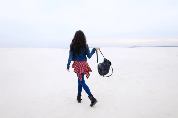 Jovem mulher caminhando sobre fundo de neve e vestindo jeans com saco . — Fotografia de Stock